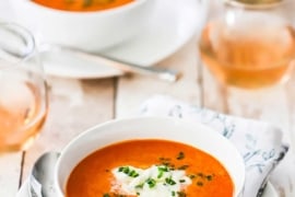 Two white soup bowls filled with carrot ginger soup sitting next to two glasses or rosé wine.