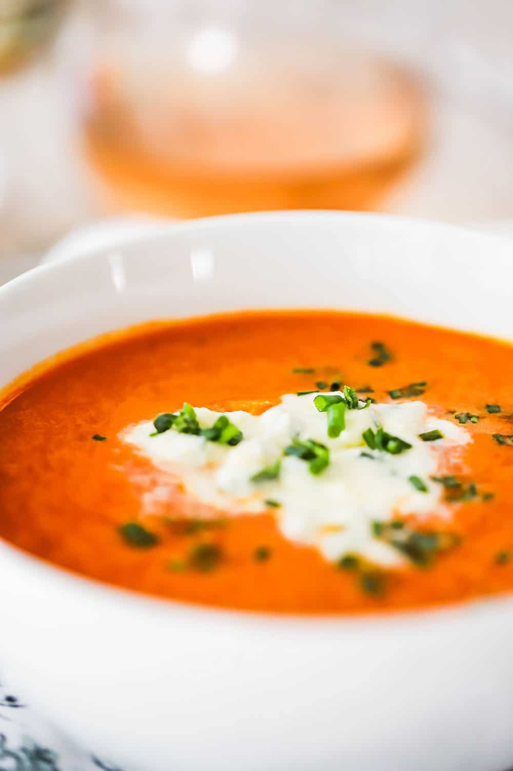 A close up view of a white bowl filled with carrot ginger soup topped with an herbed mousse.