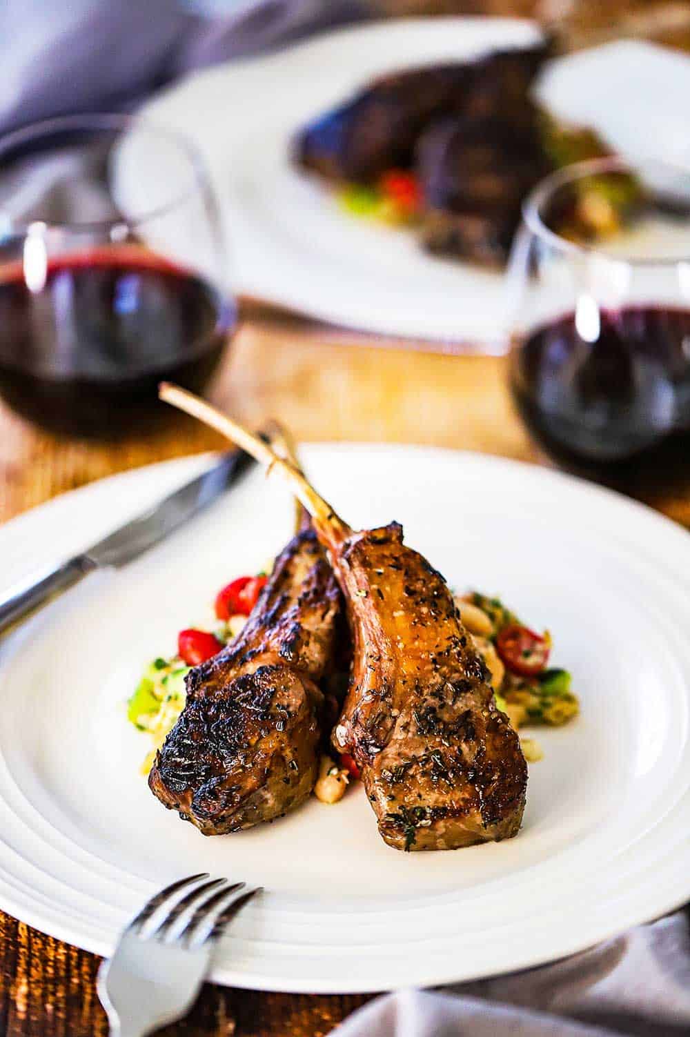 Two marinated grill lamb chops on sitting on a Greek salad on a white dinner plate.