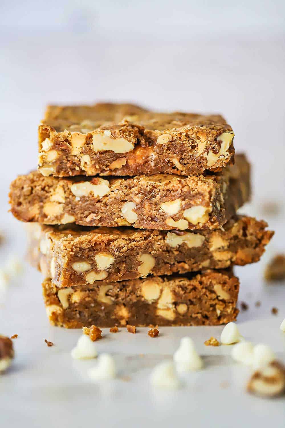 Four blondies with vanilla chips and toffee stacked on top of each other on a piece of white parchment paper.