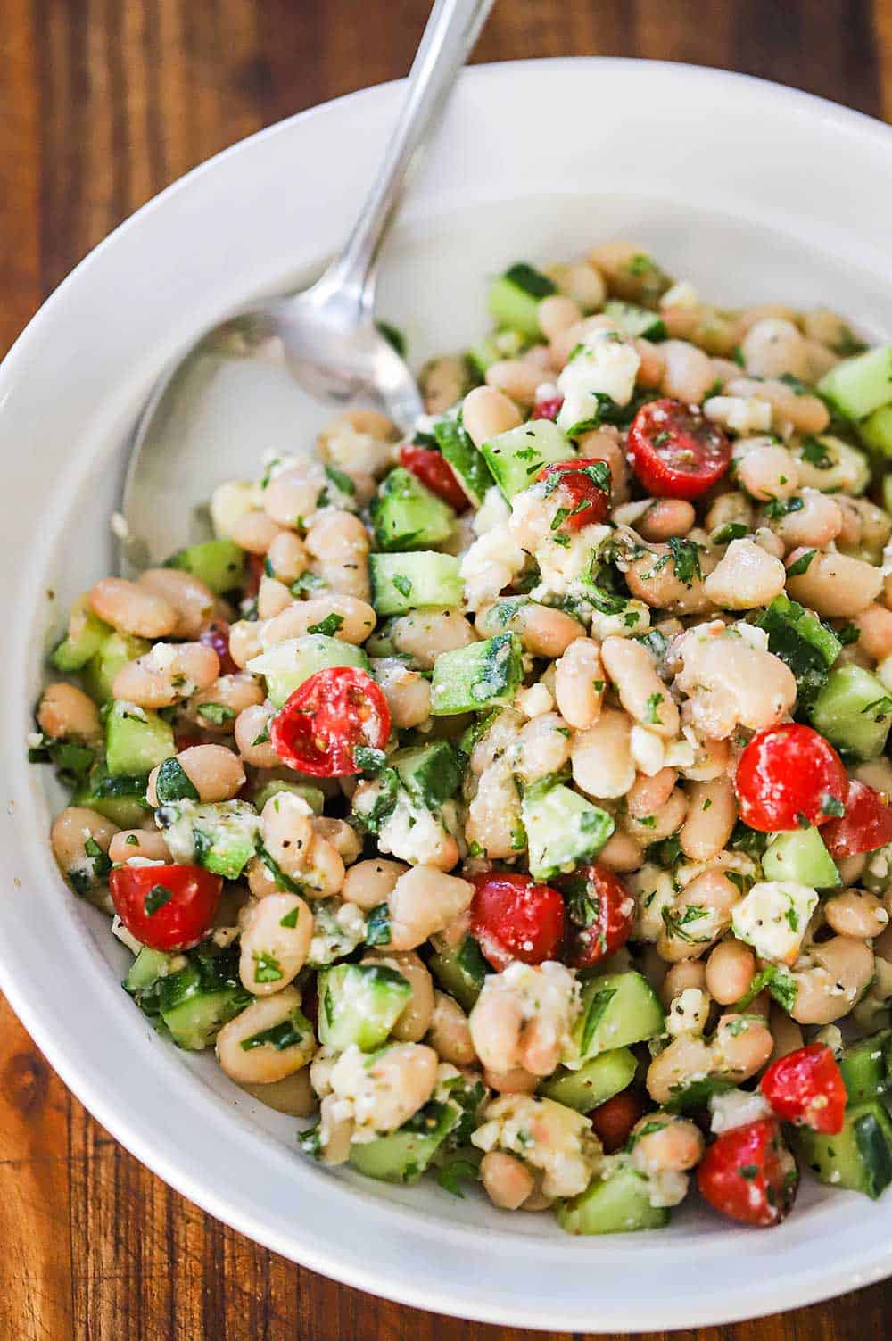 An overhead view a white serving bowl filled with a Greek white bean and cucumber salad.