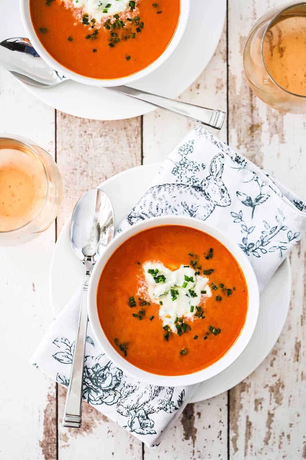 An overhead view of two white soup bowls filled with carrot ginger soup sitting next to a wine glass of Rosé.