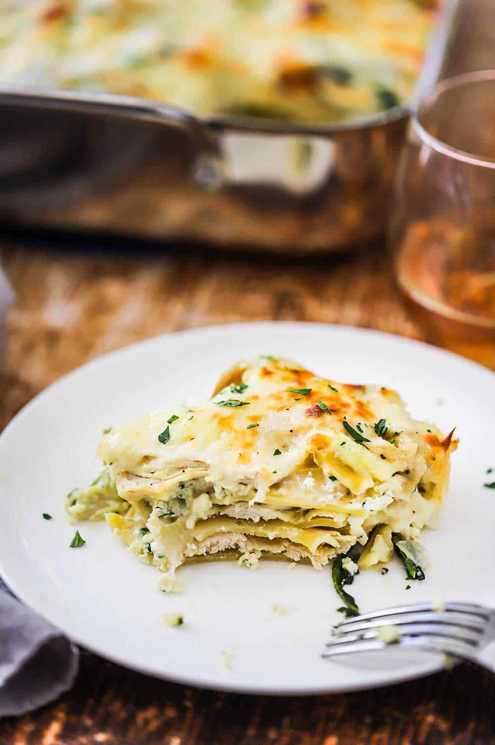 A white plate holding a serving of a white chicken lasagna with spinach with a bite taken out.