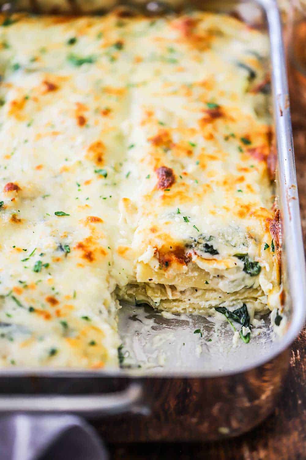 A stainless steel lasagna pan filled with chicken lasagna with the corner slice missing.