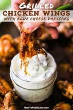 A person plunging a grilled chicken wing into a small jar filled with blue cheese dressing.