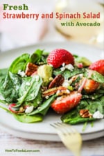 A white salad plate filled with a single serving of fresh strawberry spinach salad with avocado.