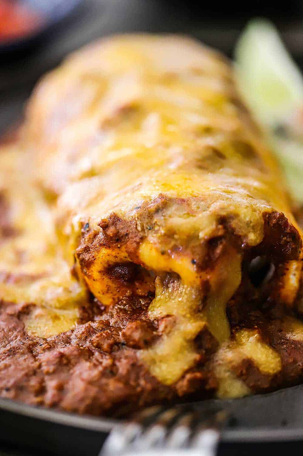 A close-up view of smothered beef burritos covered in chili con carne sauce and melted cheddar cheese.