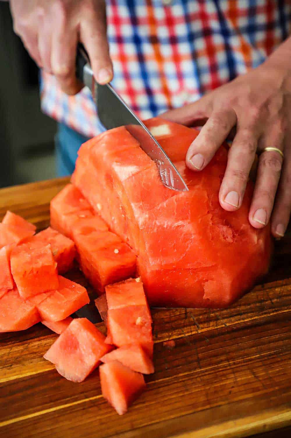 A person using a chef's knife to cut a seedless watermelon into cubes.
