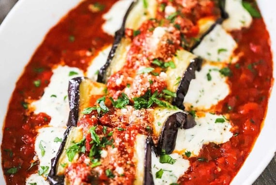 A close up view of baked eggplant rollatini with cheese oozing out the sides of each roll all nestled in a bed of marinara sauce.