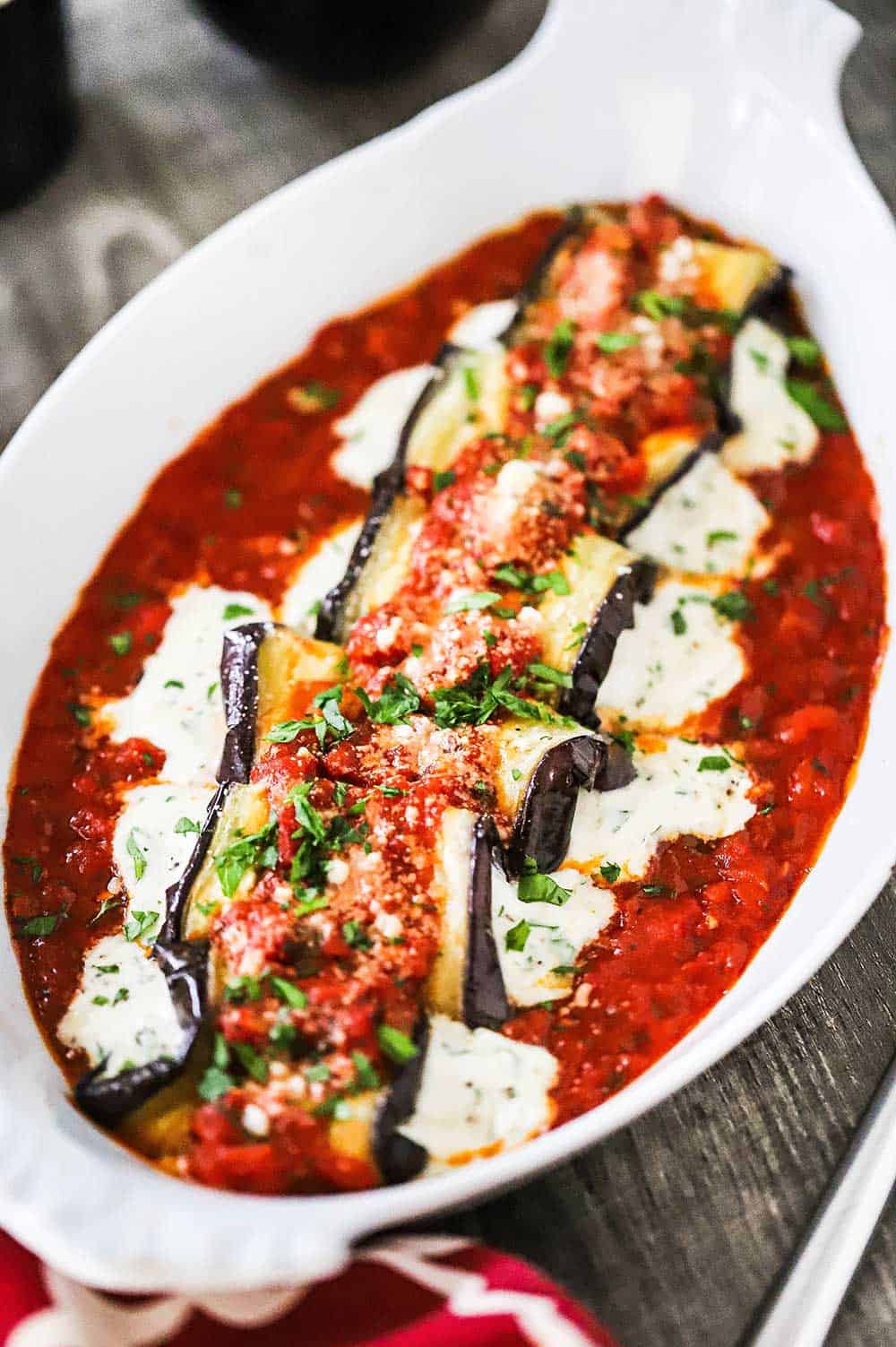 A close up view of baked eggplant rollatini with cheese oozing out the sides of each roll all nestled in a bed of marinara sauce.