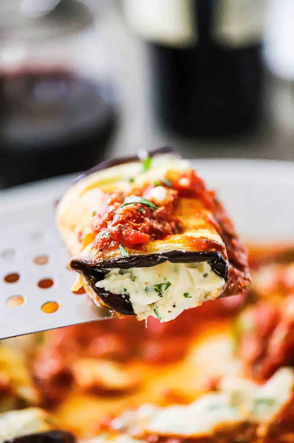 A spatula holding up a single eggplant rollatini with cheese oozing out the ends.