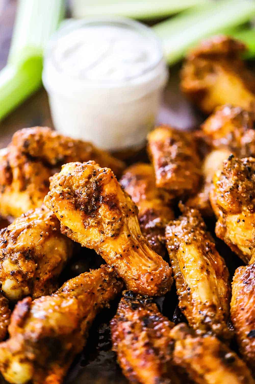 A close-up view of grilled chicken wings with buffalo sauce piled high next to a jar of blue cheese dressing.