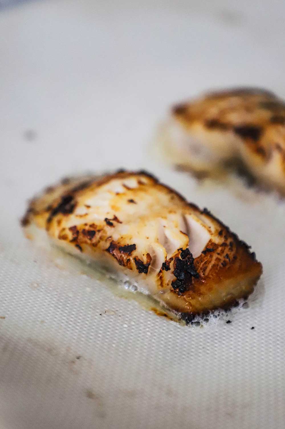 A baked strip of black cod on a silicone mat on a baking pan.