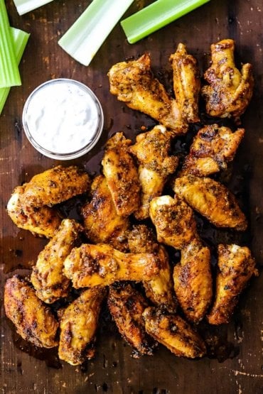 An overhead view of wings that are seasoned and grilled piled on a cutting board next to a jar of blue cheese dressing.