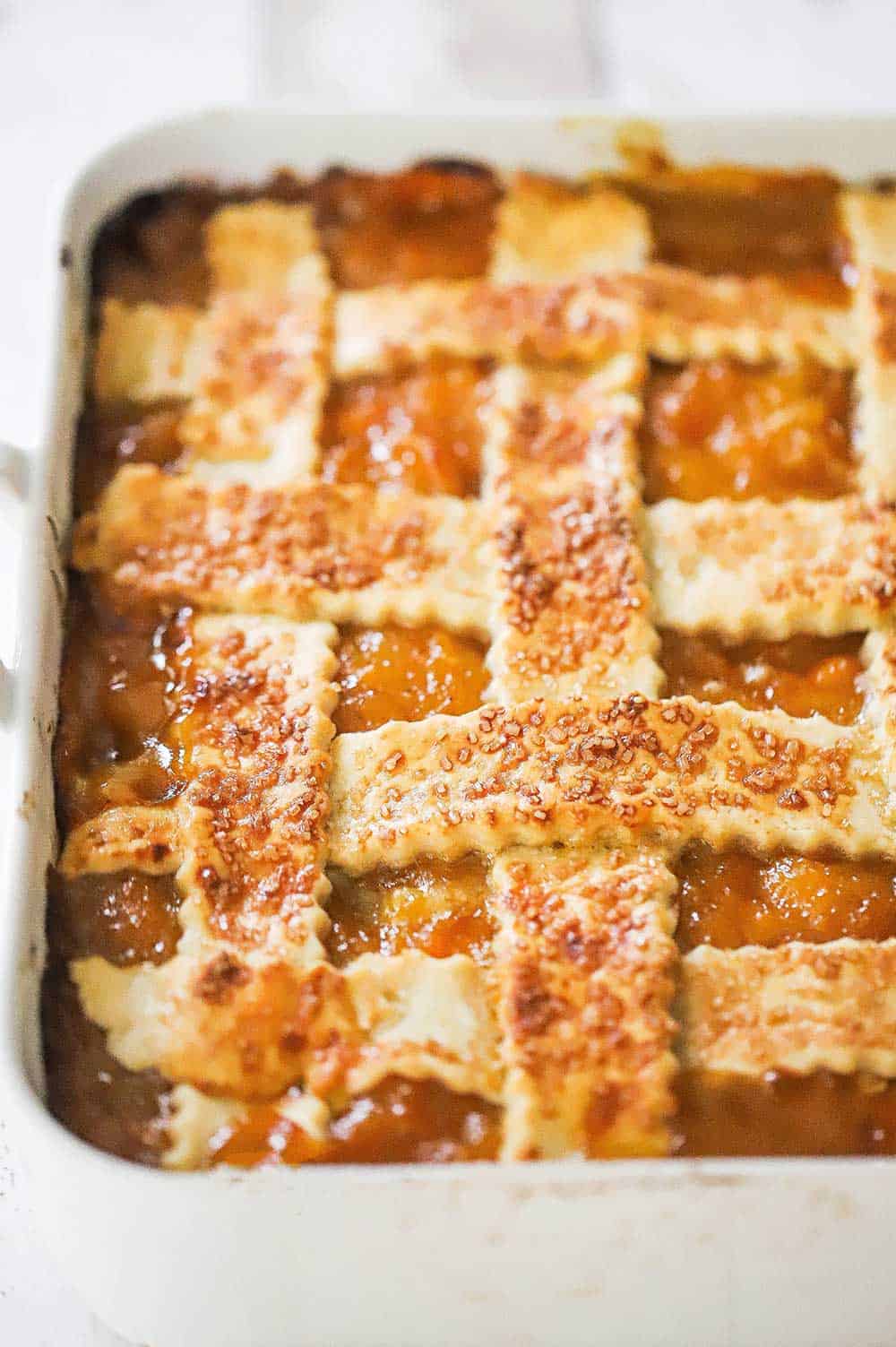 An overhead view of a baked peach cobbler that is topped with a lattice crust and topped with turbinado sugar.