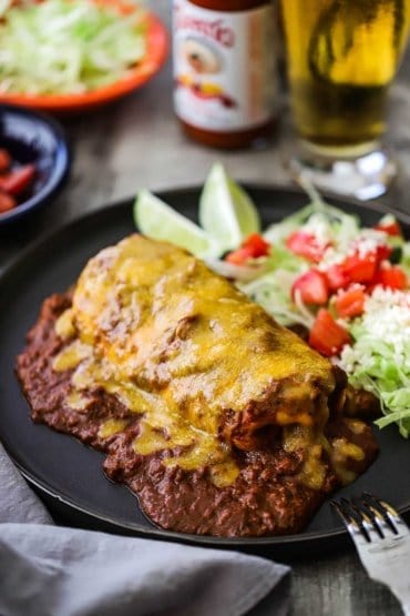 A blue plate filled with a smothered beef burrito with chili con carne sitting next to a salad topped with diced tomatoes.