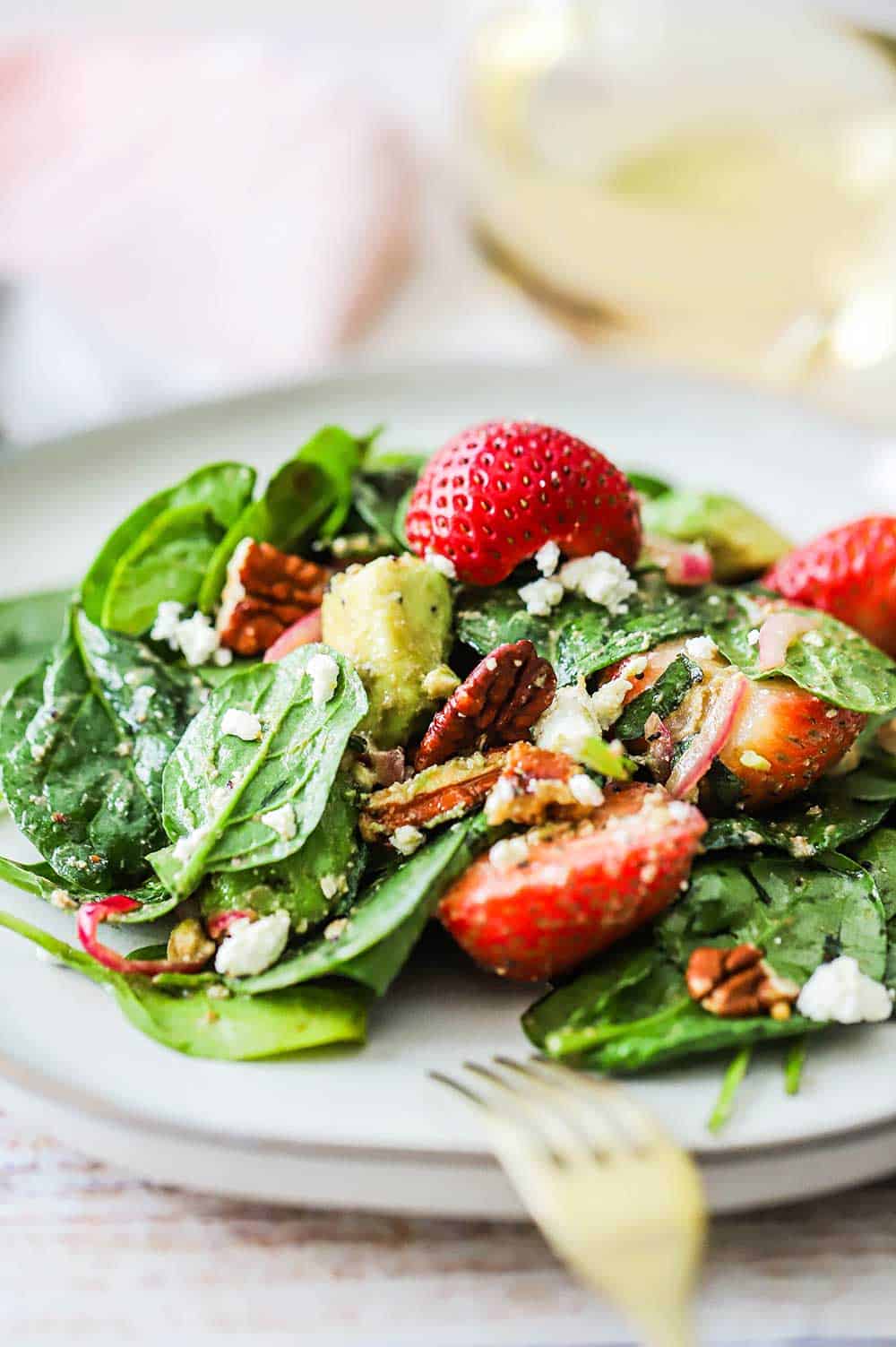A white salad plate filled with a single serving of fresh strawberry spinach salad with avocado.