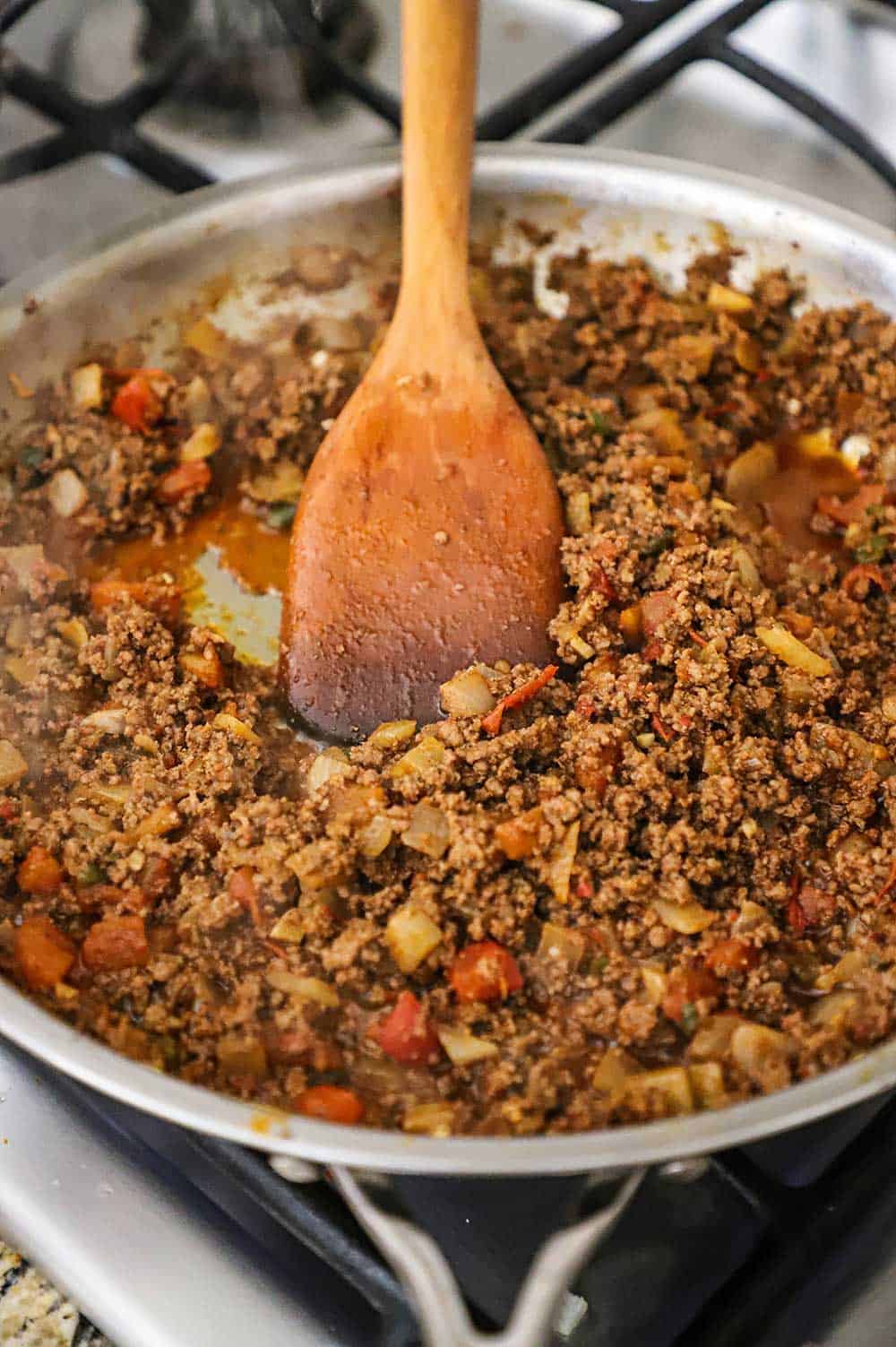 A wooden spoon inserted into a skillet filled with cooked taco meat with tomatoes.