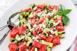 A large white oval platter filled with watermelon cucumber salad with feta and basil