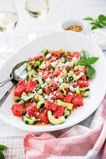 A large white oval platter filled with watermelon cucumber salad with feta and basil
