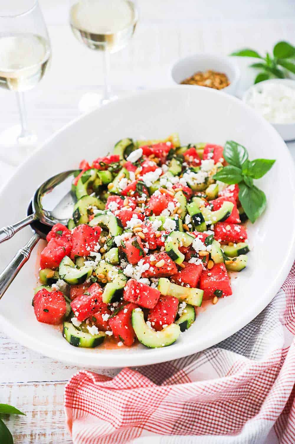 A large white oval platter filled with watermelon cucumber salad with feta and basil