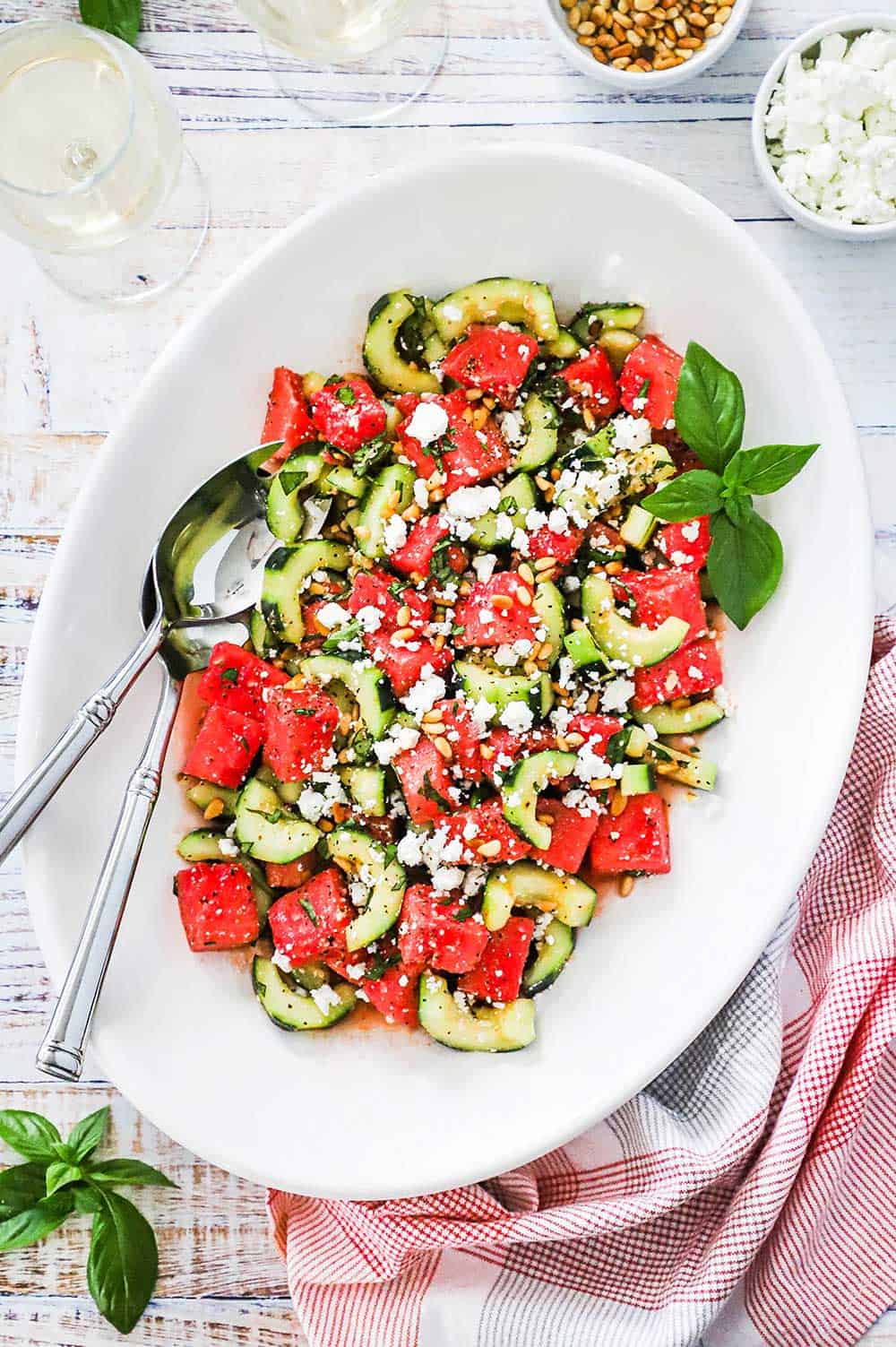 An overhead view of a large white oval platter filled with a watermelon cucumber salad with basil and feta.