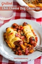 A plate filled with two grilled hot dogs wrapped in crescent rolls sitting on a bed of beef chili.