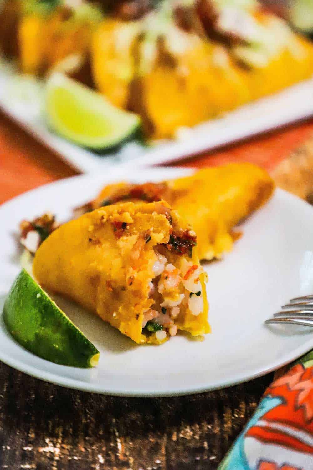 A fried shrimp taco sitting on a plate with a bite taken out of it.