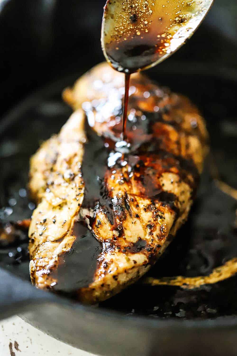 A large spoon drizzling a balsamic glaze over a seared chicken breast in a cast-iron skillet