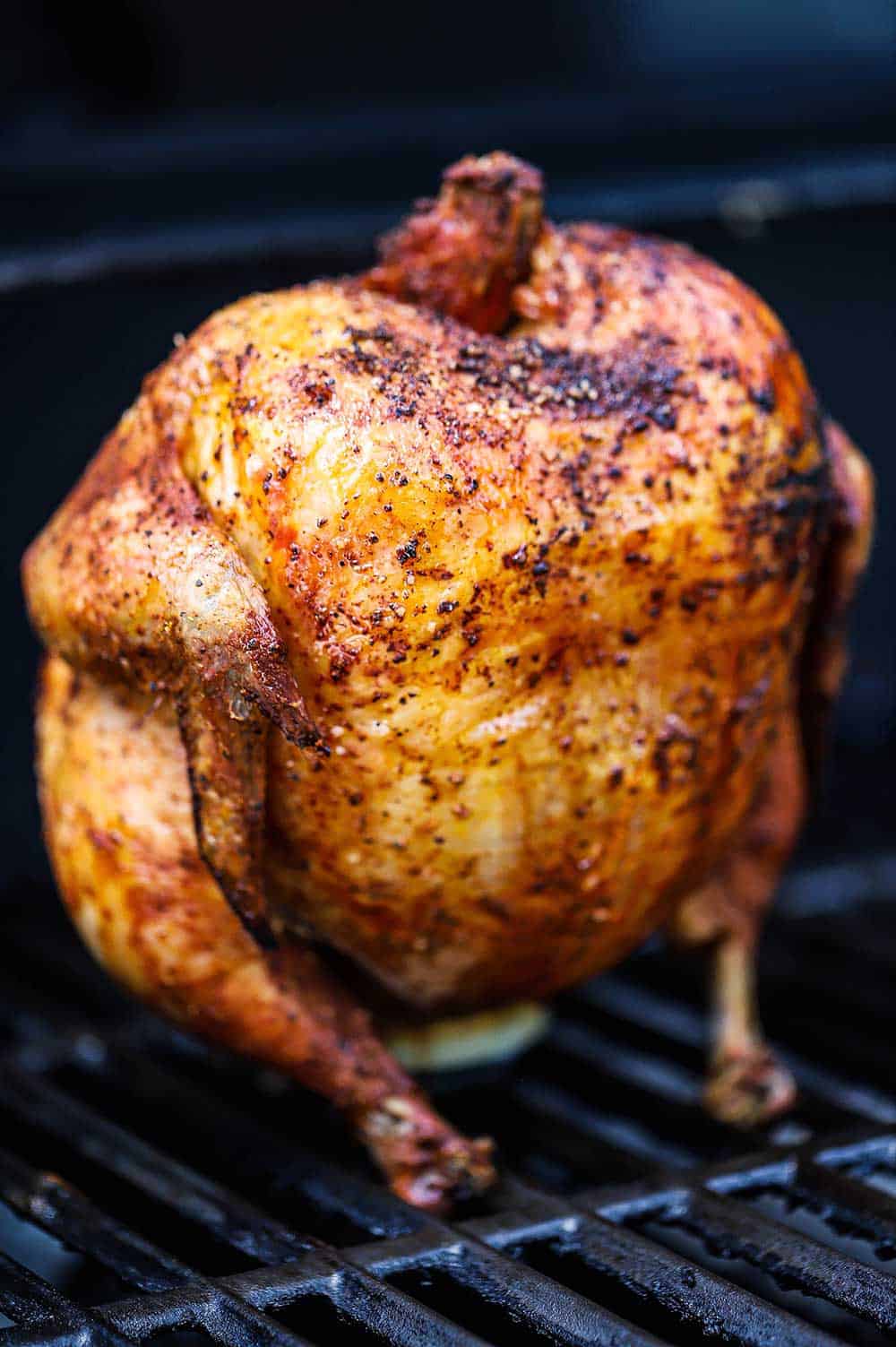 A fully cooked whole chicken that is sitting on a beer can on the grate of a gas grill.