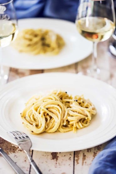 A white dinner plate filled with cacio e pepe with a fork nearby.