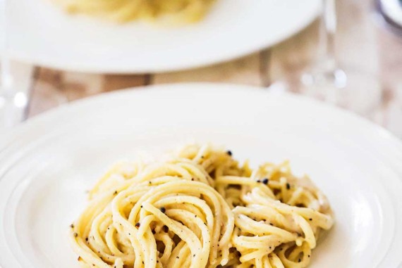A white dinner plate filled with cacio e pepe with a fork nearby.