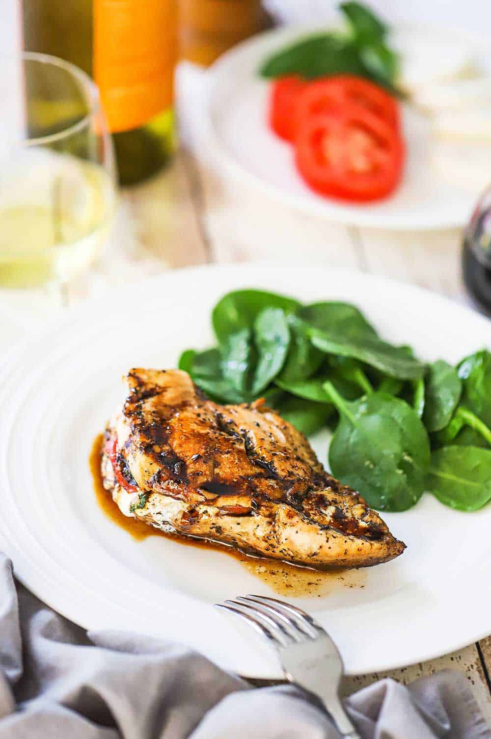 A white dinner plate filled with a caprese-stuffed chicken breast and topped with a balsamic glaze. 