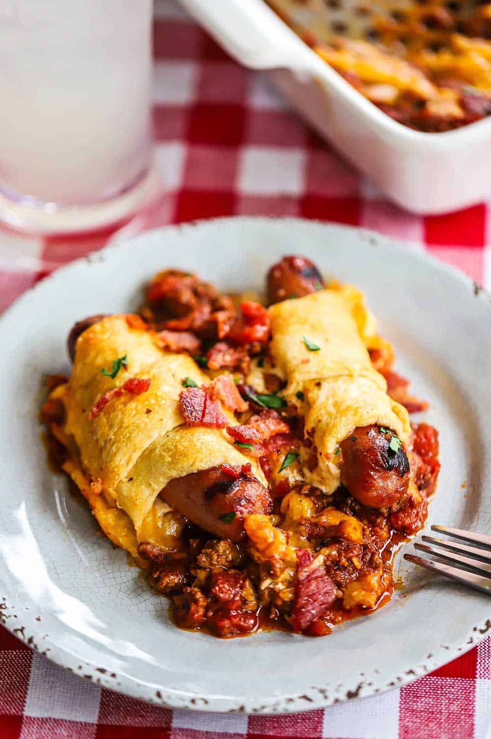 A plate filled with two grilled hot dogs wrapped in crescent rolls sitting on a bed of beef chili.