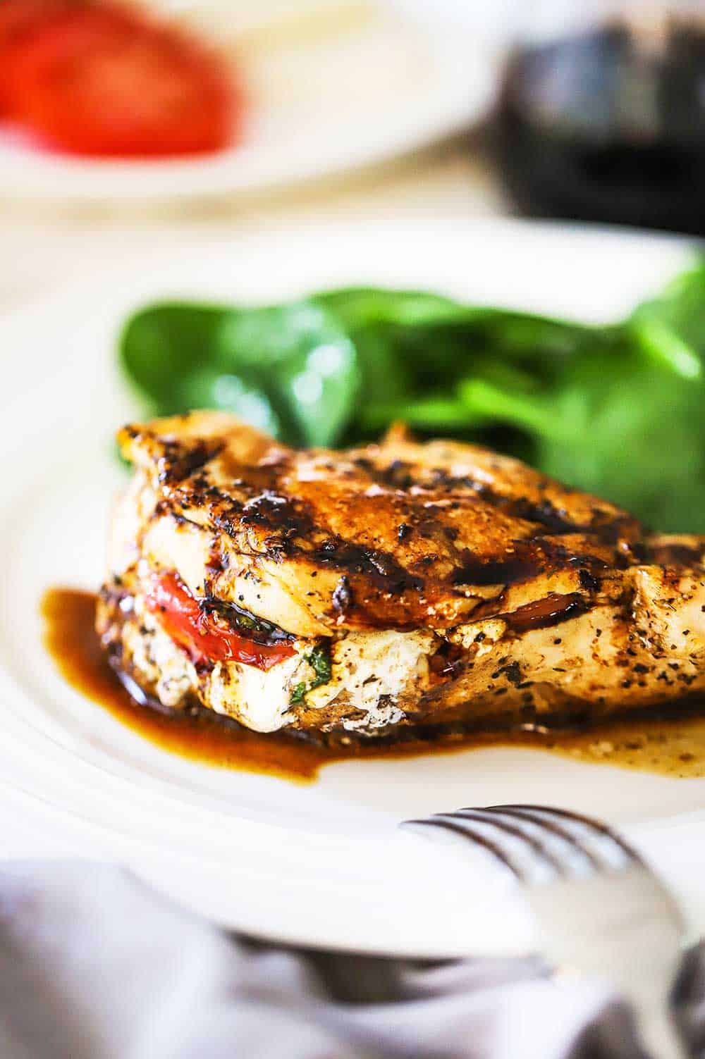 A close-up view of a caprese-stuffed chicken breast with a balsamic glaze on a white dinner plate. 