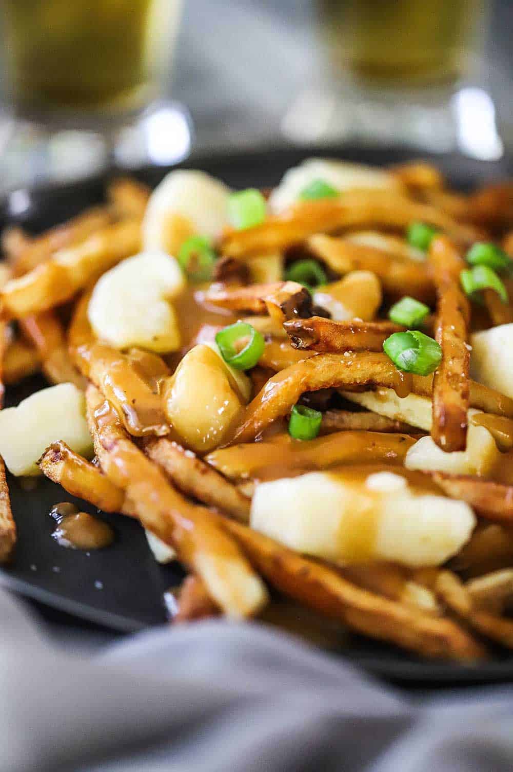 A close-up view of a black dinner plate filled with poutine and topped with chopped scallions.
