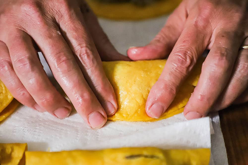 A person pressing a folded corn tortilla that has been lightly fried and stuffed with a shrimp filling.