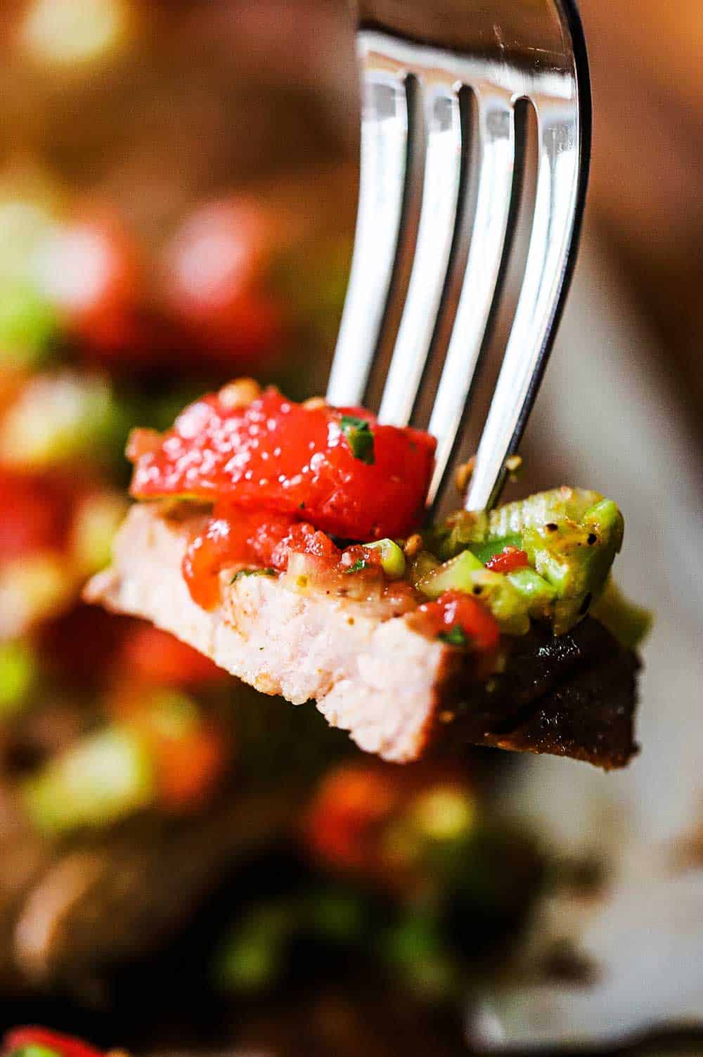 A fork holding up a bite of a grilled tri-tip steak with Santa Maria salsa.