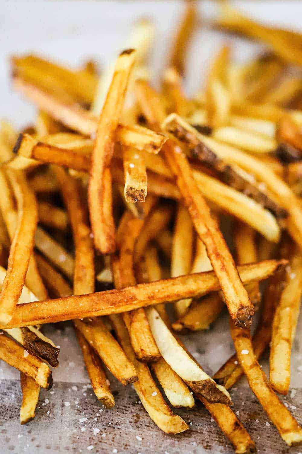 A pile of freshly made french fries sitting on paper towels and sprinkled with coarse salt.