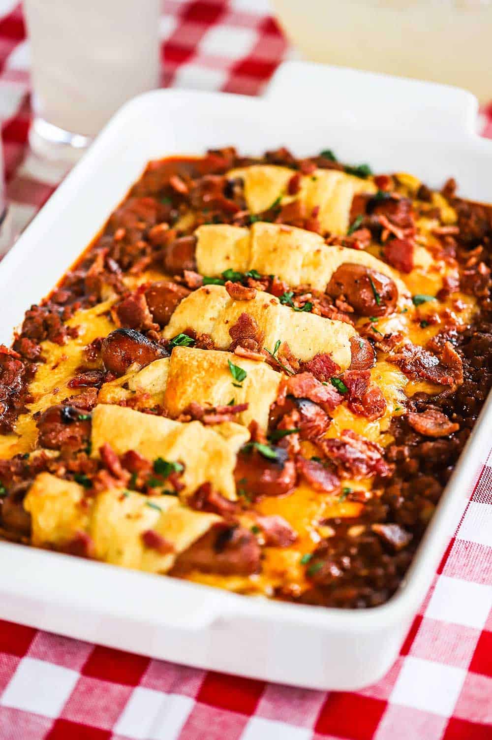 A straight-on view of a chili cheese dog casserole with crumbled bacon and chopped parsley on top.