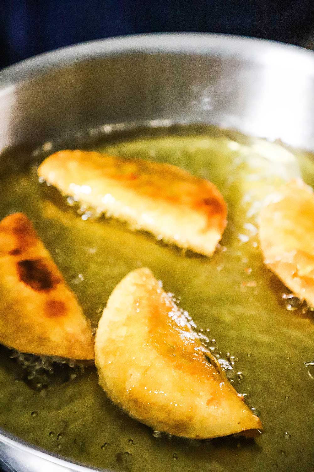 Four shrimp tacos dorados frying in a large skillet with hot oil in it.