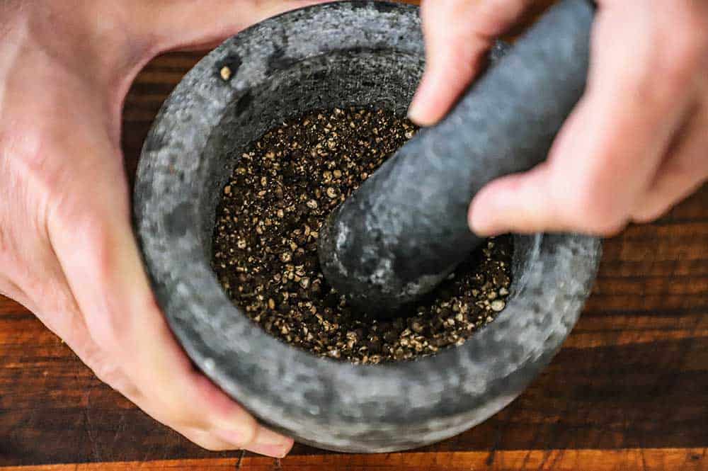 A person grinding black peppercorns in a mortar with a pestle.