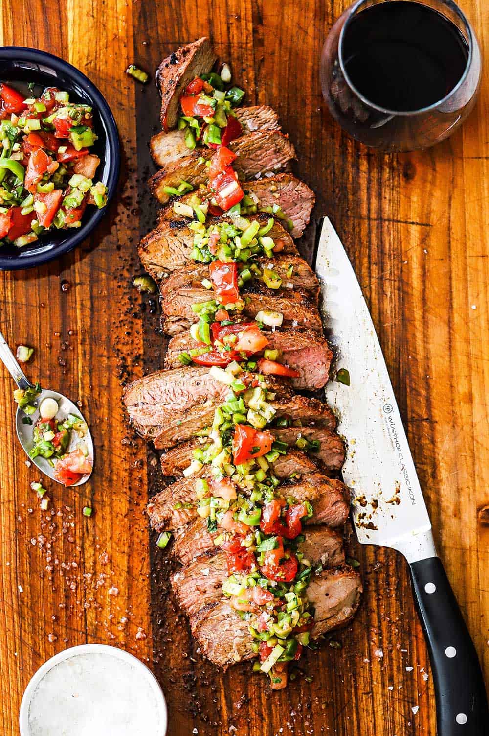 A grilled tri-tip sliced on a cutting board topped with Santa Maria salsa
