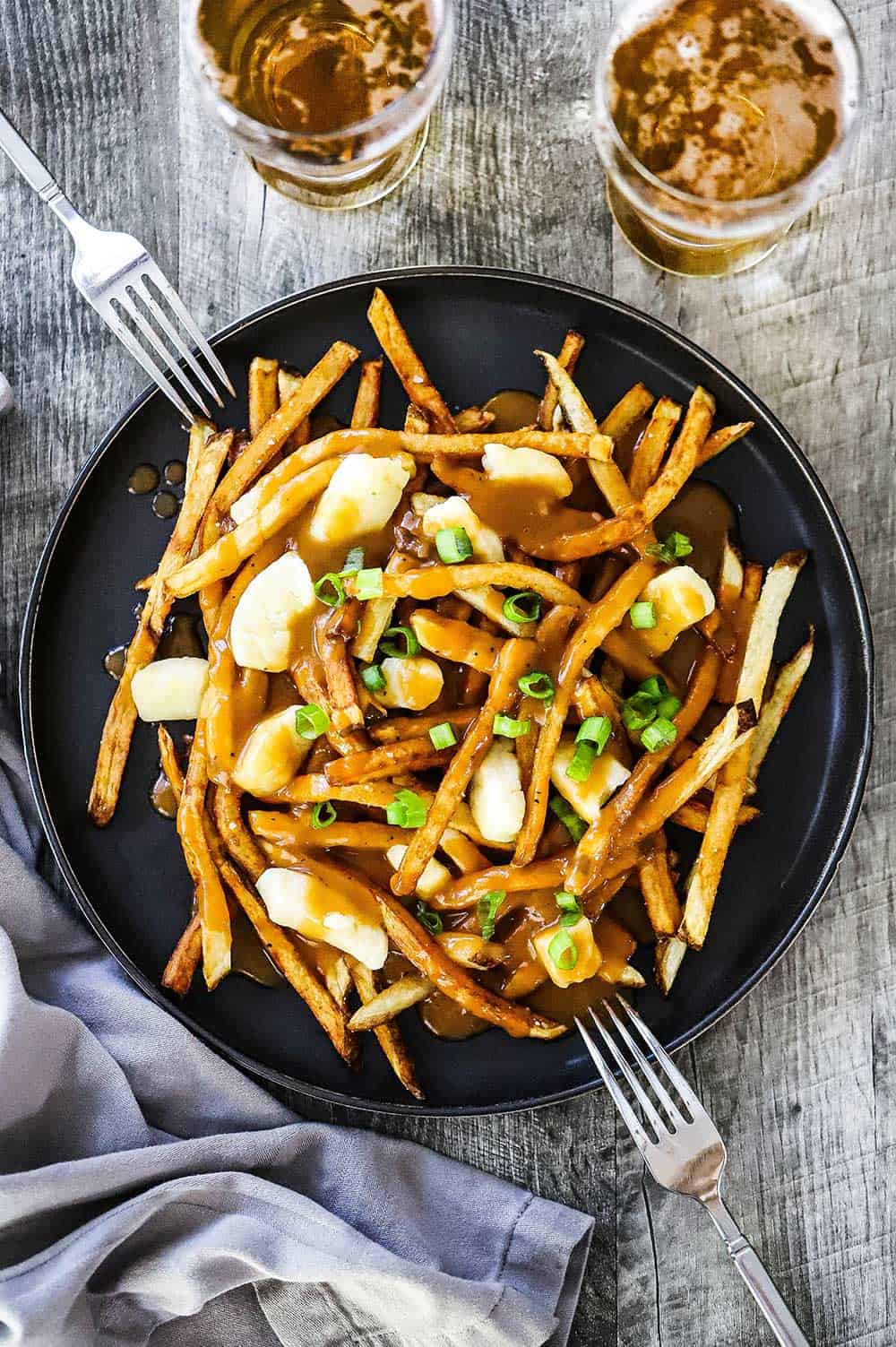 An overhead view of a black dinner plate filled with poutine with two forks on each side.