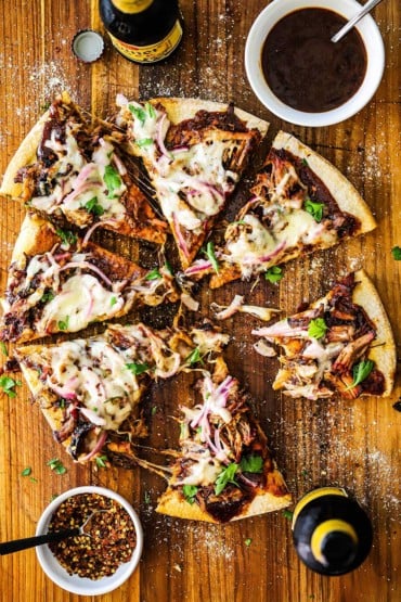 An overhead view of a grilled pulled pork pizza that has been cut into slices on a cutting board.