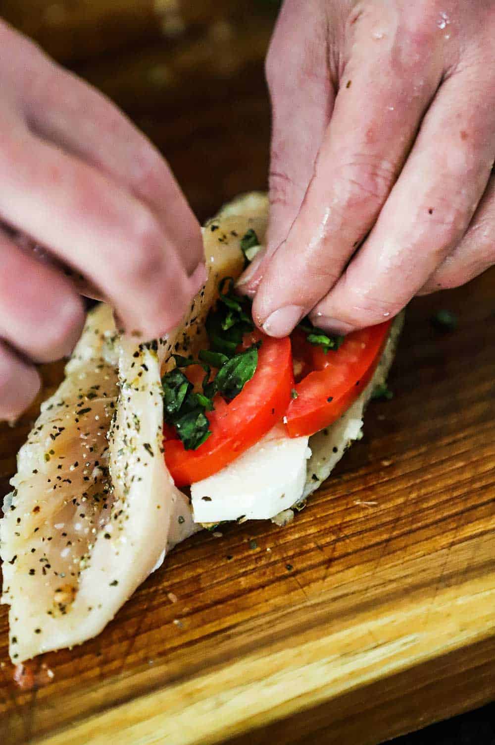 A person stuffing a chicken breast with slices of mozzarella, tomatoes, and basil. 