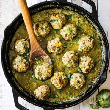 An overhead view of albondigas with salsa verde sauce in a large black cast-iron skillet with a wooden spoon in the pan.