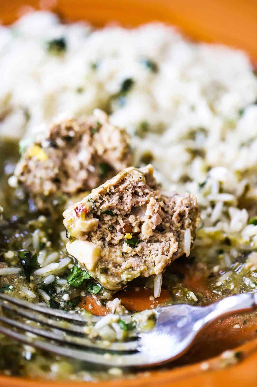 A close-up view of an albondigas meatball that is on an orange plate and is half eaten with a fork nearby.