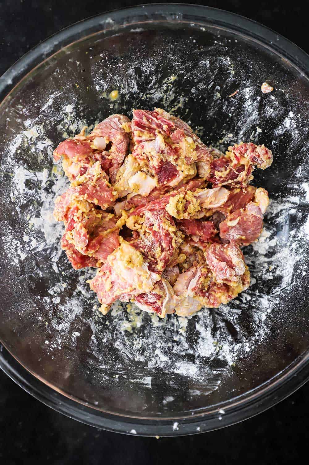 A glass bowl filled with strips of beef coated with cornstarch and flour