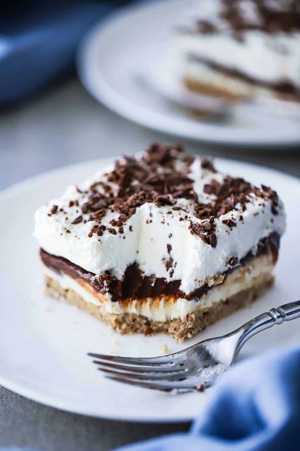 A square serving of layered chocolate delight sitting on a white plate with a bite missing.